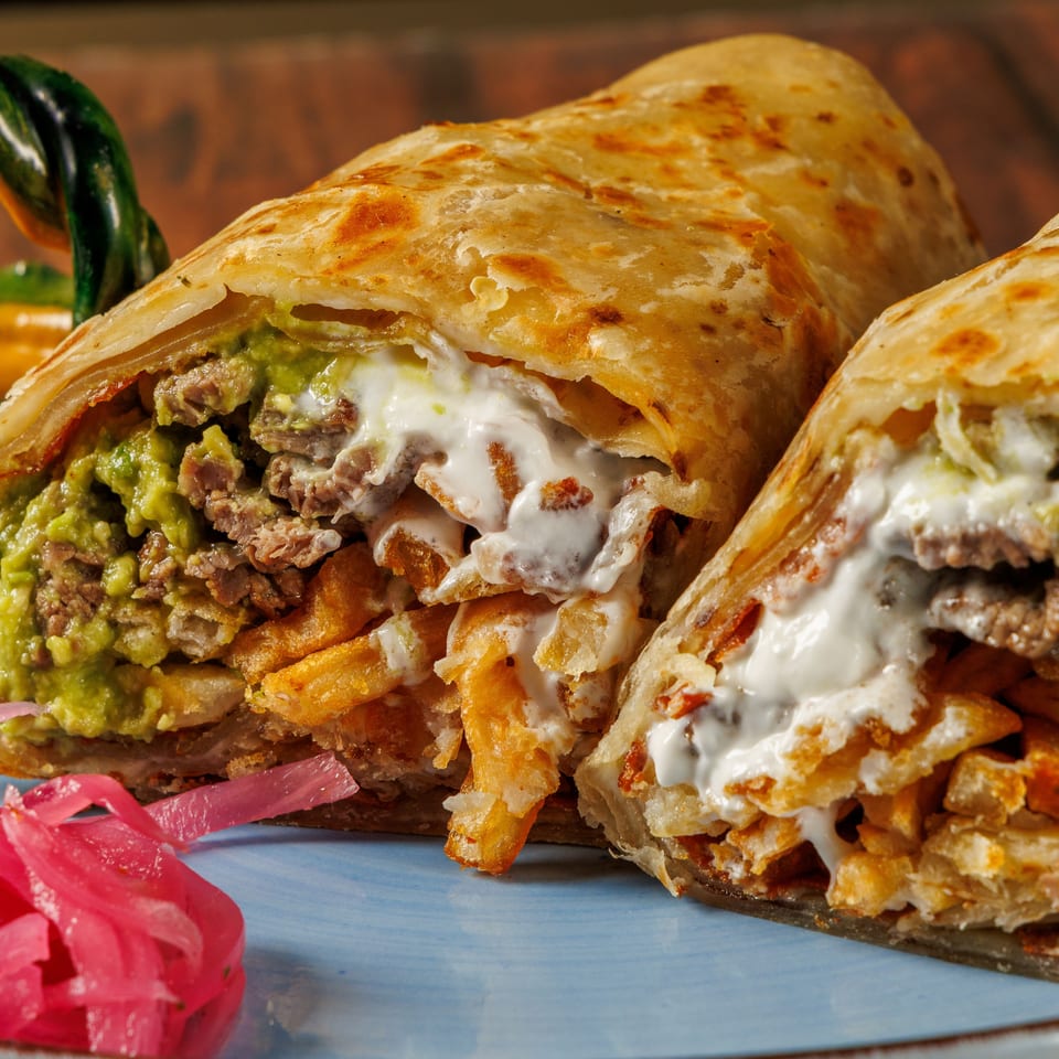 Grilled stuffed flatbreads filled with sliced meat, guacamole, crispy fries, and creamy sauce, served with pickled onions.