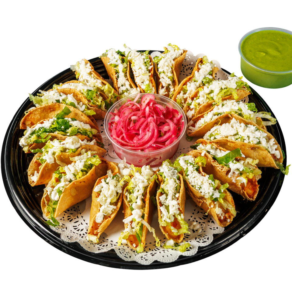 Tray of crispy tacos topped with lettuce and white cheese, surrounded by pickled onions, with green salsa on the side.