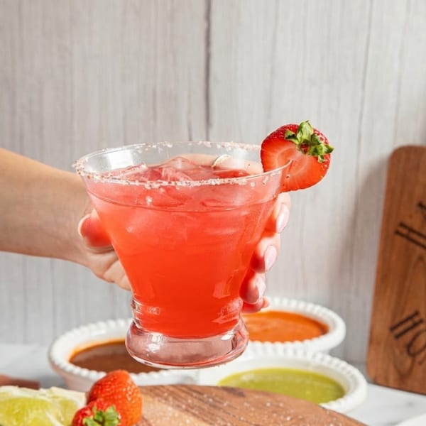 Hand holding a strawberry margarita with a salted rim, garnished with a fresh strawberry slice.