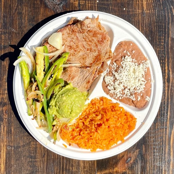 A Taqueros Mexican Restaurant plate with steak, refried beans, rice, guacamole, and grilled vegetables.