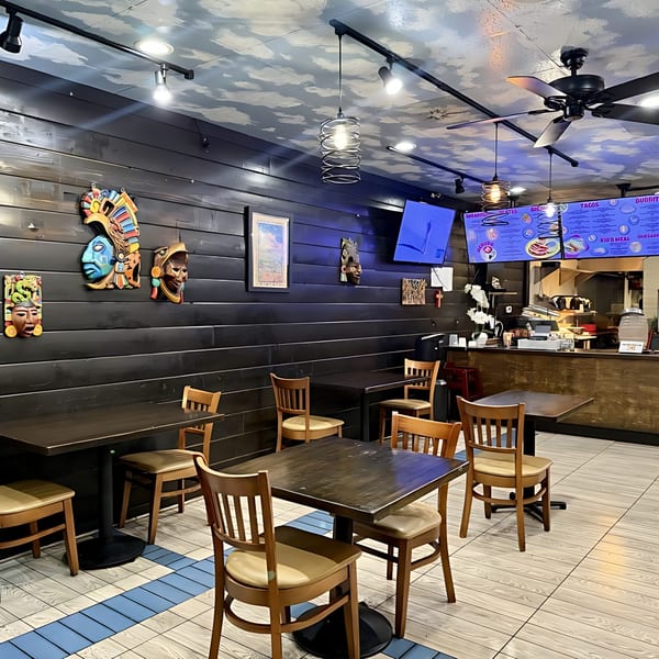 Interior of Taqueros Mexican Restaurant with dark wood tables, chairs, and decorative masks on the wall.