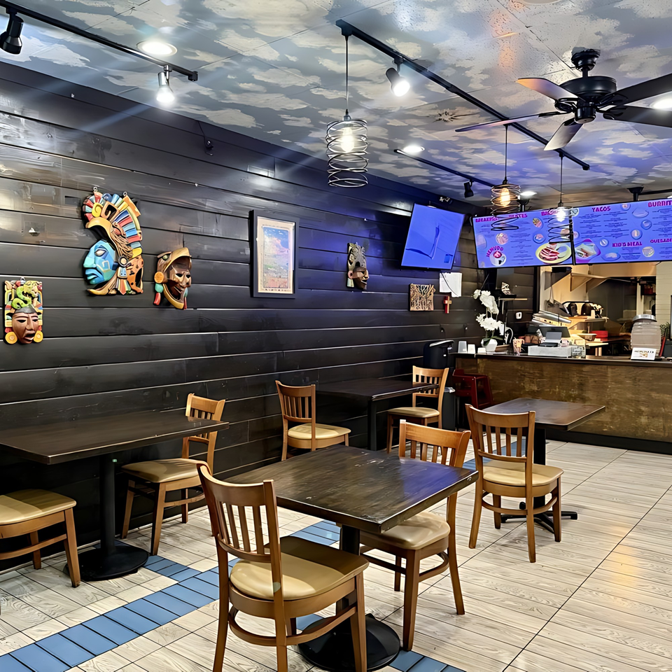 Interior of Taqueros Mexican Restaurant with dark wood tables, chairs, and decorative masks on the wall.