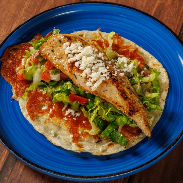 Grilled chicken breast with crumbled cheese, lettuce, and salsa on a tortilla, served on a blue plate.