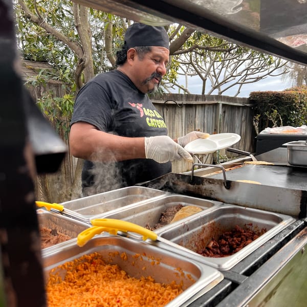 A Taqueros Mexican Restaurant chef prepares food on a grill with rice and meat in serving trays.
