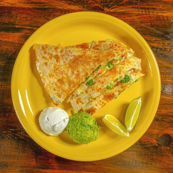 Taqueros Mexican Restaurant's quesadilla with guacamole, sour cream, and lime wedges on a yellow plate.