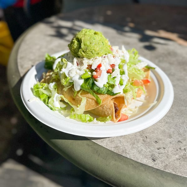 Crispy taquitos topped with guacamole, lettuce, cheese, tomatoes, and sour cream on a white plate.