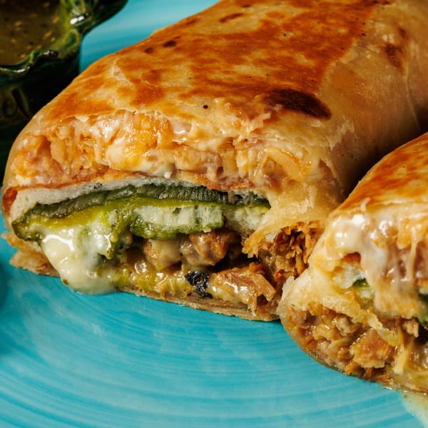 Close-up of a sliced Taqueros Mexican Restaurant burrito, revealing melted cheese, green sauce, and meat filling.