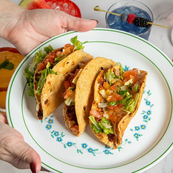 Hands holding a plate of three Taqueros Mexican Restaurant tacos with lettuce and pico de gallo.