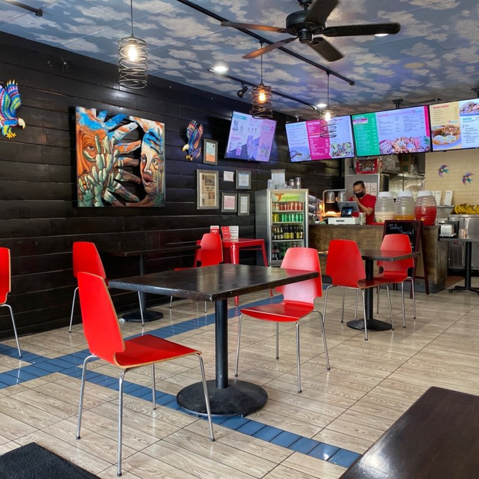 Interior of Taqueros Mexican Restaurant with red chairs, dark tables, and a cloud-painted ceiling.